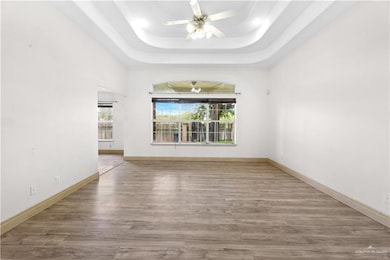 Unfurnished living room with ceiling fan, wood finished floors, and a tray ceiling