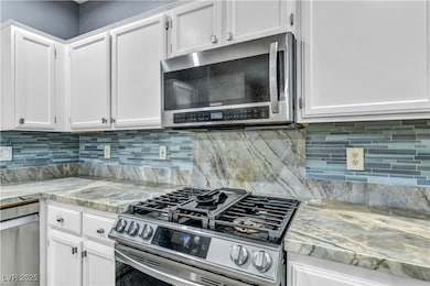 Kitchen featuring white cabinetry, stainless steel appliances, tiled backsplash, and quartz countertops