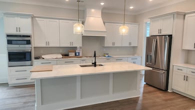 Kitchen with appliances with stainless steel finishes, premium range hood, light countertops, a center island with sink, and pendant lighting