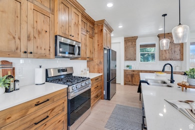 Kitchen with stainless steel appliances, decorative backsplash, quartz countertops, decorative light fixtures, and light wood-style flooring