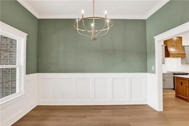 Unfurnished dining area with light wood-type flooring, a chandelier, ornamental molding, a wainscoted wall, and a decorative wall