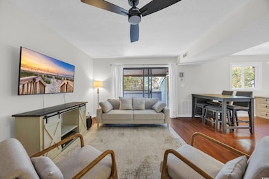 Living area with a ceiling fan, wood finished floors, healthy amount of natural light, and a textured ceiling