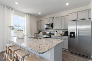Kitchen with stainless steel appliances, a sink, gray cabinetry, dark wood-style floors, and a breakfast bar area