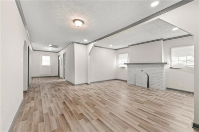 Unfurnished living room featuring ornamental molding, plenty of natural light, wood finished floors, a textured ceiling, and baseboards