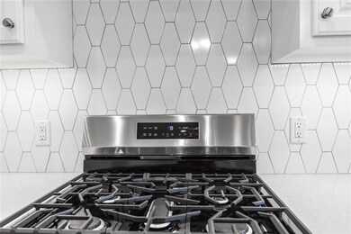 Kitchen view of light stone counters, backsplash, stainless steel gas stove, and white cabinets