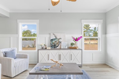 Living area featuring a decorative wall, wainscoting, healthy amount of natural light, light wood-style flooring, and ceiling fan