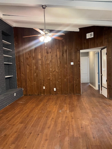 Unfurnished living room featuring dark wood-type flooring, beam ceiling, wooden walls, and a ceiling fan