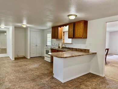 Kitchen with electric stove, a textured ceiling, a peninsula, dark countertops, and brown cabinetry