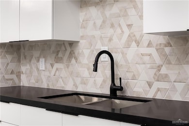 Kitchen view of white cabinetry, dark countertops, backsplash, and modern cabinets