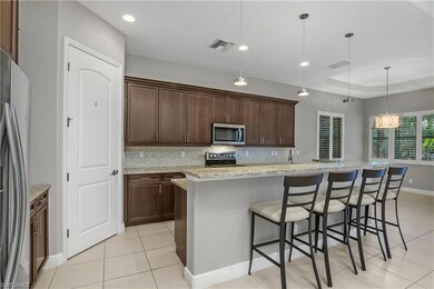 Kitchen with a breakfast bar, decorative backsplash, light stone countertops, hanging light fixtures, and a center island with sink