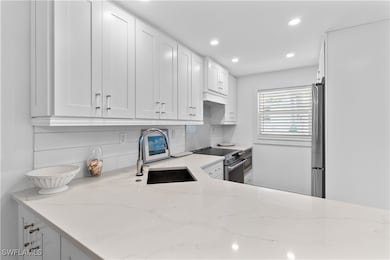Kitchen featuring tasteful backsplash, white cabinets, light stone countertops, appliances with stainless steel finishes, and sink