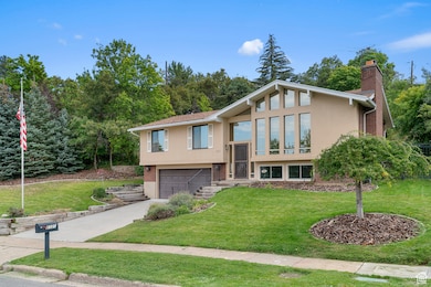 Raised ranch with stucco siding, a front lawn, a chimney, driveway, and a garage