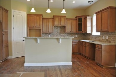 gourmet kitchen with granite countertops, island, pendant lighting, sand and finish hardwood floors and corner pantry