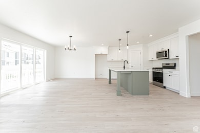 Kitchen featuring stainless steel appliances, light wood-style floors, light countertops, pendant lighting, and a center island with sink