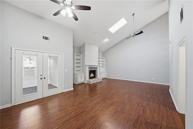 Unfurnished living room featuring a ceiling fan, high vaulted ceiling, a skylight, dark wood finished floors, and a brick fireplace