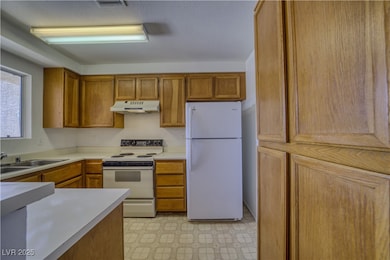 Kitchen with white appliances, brown cabinetry, light countertops, under cabinet range hood, and light flooring