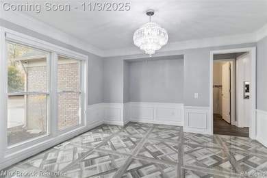 Unfurnished dining area with wainscoting, a chandelier, crown molding, and a decorative wall