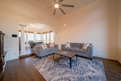 Living area with a decorative wall, wainscoting, arched walkways, dark wood flooring, and decorative columns