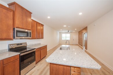 Kitchen featuring stainless steel appliances, a kitchen island with sink, brown cabinets, light wood finished floors, and recessed lighting