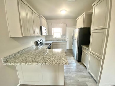 Kitchen featuring stainless steel appliances, a peninsula, light stone countertops, and light wood finished floors