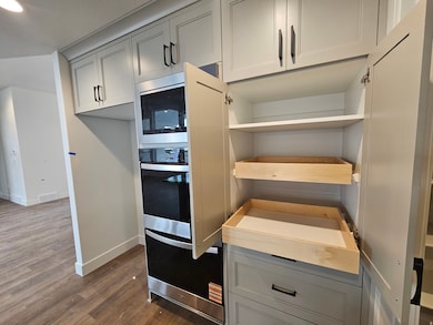 Kitchen with gray cabinetry, dark wood finished floors, stainless steel microwave, and light countertops