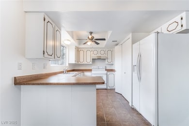 Kitchen with white appliances, a peninsula, white cabinets, a tray ceiling, and under cabinet range hood
