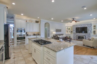 Gas cooktop and prep sink in the island overlooking the living area with tile fireplace and glass-doored built-ins.  