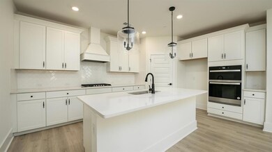 Kitchen with custom exhaust hood, a sink, stainless steel double oven, light wood finished floors, and tasteful backsplash