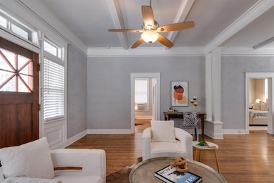 Living area with healthy amount of natural light, wood finished floors, ceiling fan, beam ceiling, and ornamental molding