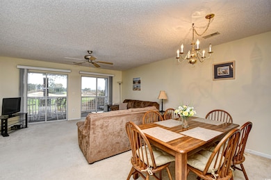 Dining space with a chandelier, light colored carpet, a textured ceiling, and ceiling fan
