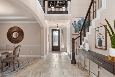 The view toward the front door highlights the classic travertine tile, arched openings, and crown molding.  The office is to the right by the front door.  To the left is the hallway to the downstairs secondary bedroom and full bathroom.  The large open dining room is just to the left.  The detail and attention given to this area of the home will impress.