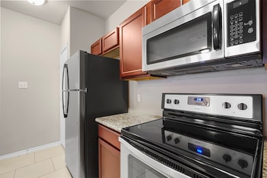 Kitchen featuring stainless steel appliances, light tile patterned floors, and light stone countertops