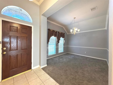 Carpeted entrance foyer featuring ornamental molding, healthy amount of natural light, vaulted ceiling, tile patterned floors, and a chandelier