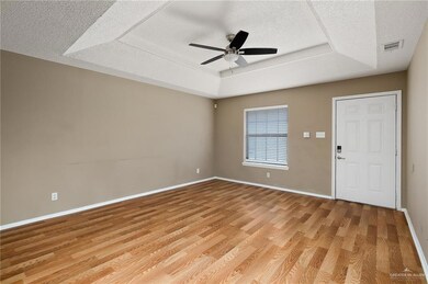 Unfurnished room featuring a raised ceiling, ceiling fan, light hardwood / wood-style flooring, and a textured ceiling