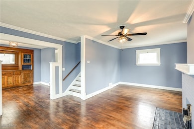Unfurnished living room with ornamental molding, dark wood finished floors, a ceiling fan, stairway, and decorative fireplace.