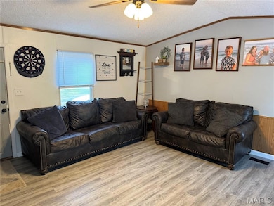 Living area with a textured ceiling, ceiling fan, a wainscoted wall, crown molding, and wood finished floors