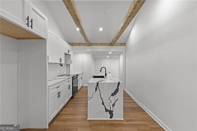 Kitchen with black electric range oven, white cabinetry, a sink, wood finished floors, and light stone countertops