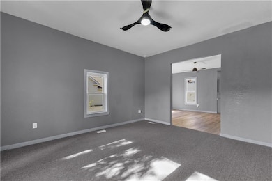 Carpeted Living room open to dining room  with a ceiling fan and baseboards