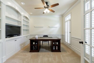 Bright and spacious home office on the main level featuring custom built-in cabinetry, French doors, and abundant natural light through plantation-shuttered windows.