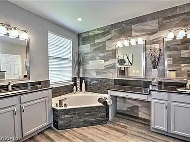 Full bath with two vanities, light wood finished floors, tile walls, a garden tub, and recessed lighting