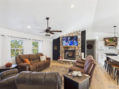Living room with vaulted ceiling, a stone fireplace, light wood-style floors, ceiling fan, and recessed lighting