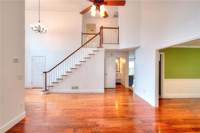View of staircase from living room featuring a ceiling fan, a towering ceiling, stairs, wood finished floors, and a chandelier