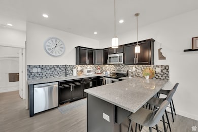 Kitchen featuring light stone countertops, decorative backsplash, a breakfast bar, appliances with stainless steel finishes, and light wood-type flooring