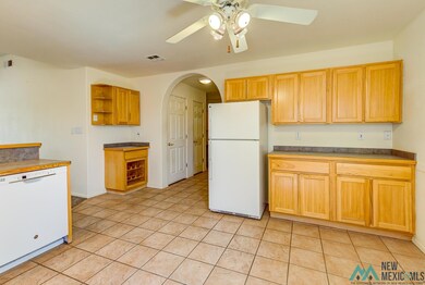 Kitchen with white appliances, arched walkways, open shelves, and light tile patterned flooring