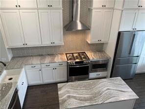 Kitchen featuring appliances with stainless steel finishes, wall chimney range hood, and white cabinets