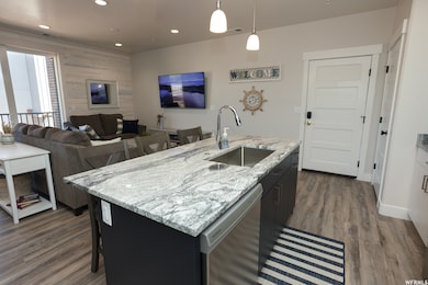 Kitchen with a breakfast bar area, light stone counters, hanging light fixtures, dishwashing machine, and an island with sink