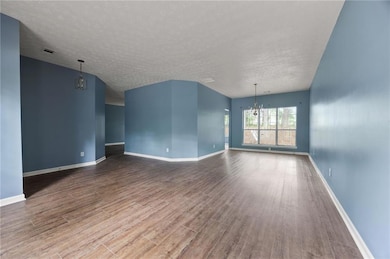 Unfurnished living room featuring a chandelier, wood finished floors, a textured ceiling, and baseboards