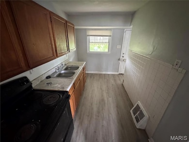 Kitchen with black electric range, light countertops, brown cabinetry, and dark wood finished floors