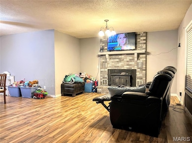 Living room featuring a textured ceiling, wood finished floors, a fireplace, and a chandelier