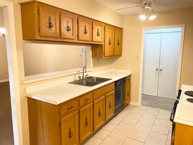 Kitchen with light tile floors, white stove, sink, black dishwasher, and ceiling fan